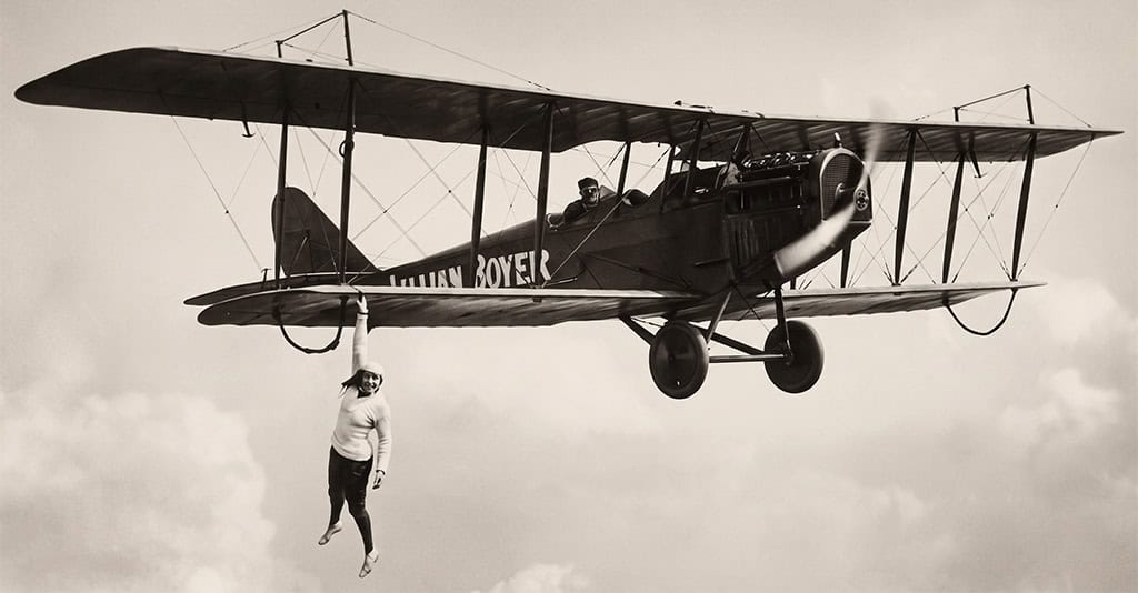 Lillian Boyer hands from the wing of a plane in a 1920s barnstorming stunt.